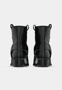 Cizme negre până la gleznă cu un finisaj din piele netedă, având curele duble cu accesorii metalice și un toc jos, masiv.