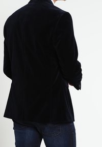 Mörk sammet blazer med en mjuk textur, skräddarsydd passform och slagkrage. Har en enkel slits och knappaccentuationer för en polerad look.