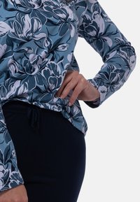 Pitkähihainen kukkakuosisetti sinisen ja valkoisen sävyissä, yhdistettynä tummiin joustaviin housuihin; sisältää pyöreän pääntien ja löysän istuvuuden.