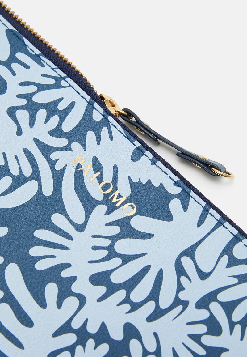 Blue bag with coral pattern, made of textured material. Gold "PALOMO" logo. Features a gold zipper and a navy accent around the edge.