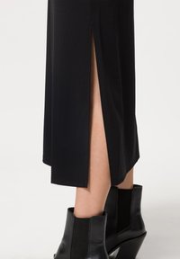 Vestido negro con una abertura lateral, hecho de un material suave. Acompañado de botas negras de tobillo con detalles acanalados y un tacón geométrico.