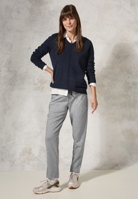 Marinblått stickat tröja över en vit skjorta med krage, kombinerat med grå joggers och ljusa sneakers. Slät textur, avslappnad design.