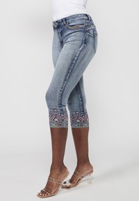 Hellblaue Denim-Capri-Jeans mit dekorativen gestickten Mustern am Saum. Sie verfügen über eine taillierte Passform und Kontrastnähte, sowie Taschen.