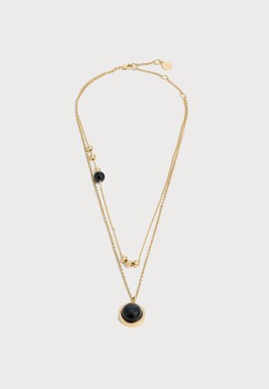Collier chaîne en or à double couche avec pendentifs en pierre noire ronde et petites perles dorées sur fond blanc.