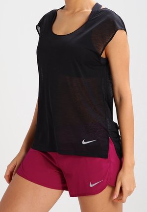 Kobieta w czarnym sportowym topie bez rękawów i magentowych krótkich spodenkach do biegania, obie z małymi odblaskowymi logo Nike po lewej stronie.