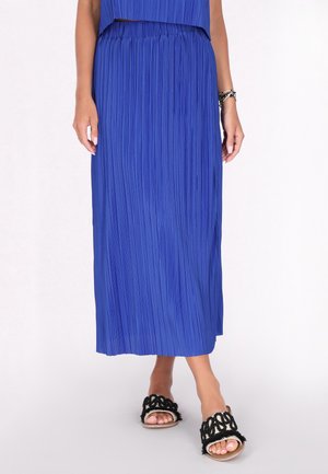Blauwe geplooide maxi rok met een elastische tailleband, gecombineerd met zwarte sandalen met een decoratief geweven ontwerp. Soepele stoftextuur.