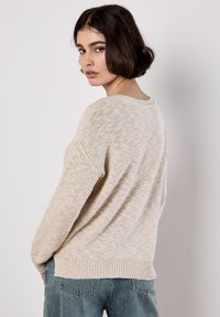 Beige gebreide trui met een losse pasvorm, ribbelzoom en brede mouwen, met een textuurpatroon en een ronde hals.