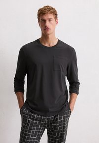 Zwarte lange mouwen T-shirt met een ronde hals en een borstzak, gecombineerd met gestreepte grijze broek met een ruitpatroon.