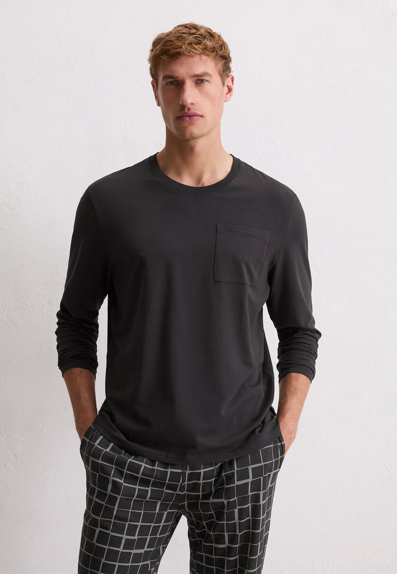 Zwarte lange mouwen T-shirt met een ronde hals en een borstzak, gecombineerd met gestreepte grijze broek met een ruitpatroon.