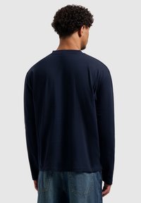 Dunkelblaues Langarm-T-Shirt aus weichem Stoff, mit Rundhalsausschnitt und legerer Passform, kombiniert mit hellblauen Jeansshorts.