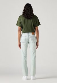 Kortermet olivengrønn T-skjorte kombinert med lyseblå rettstilte jeans og hvite joggesko; har et brunt lærfremre merke.