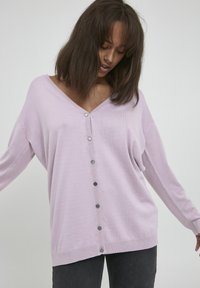 Lila Strickjacke aus weichem Strickstoff, mit V-Ausschnitt, überschnittenen Schultern und sechs dunklen Knöpfen an der Vorderseite. Lockere Passform.