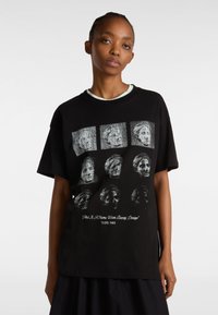 Camiseta de algodón negra con un estampado gráfico de rostros en un patrón de cuadrícula en el frente. Corte relajado con mangas cortas y cuello redondo.