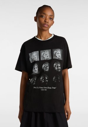 Black cotton t-shirt featuring a graphic print of faces in a grid pattern on the front. Relaxed fit with short sleeves and crew neckline.