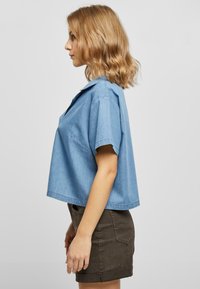 Lyseblå kortermet chambray-skjorte med krage, cropped design og lett tekstur, kombinert med et mørkebrunt tettsittende skjørt.