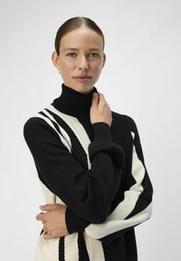 Sort og hvid stribet turtleneck sweater med ribbede manchetter og krave, prydet med et iøjnefaldende geometrisk mønster, blød tekstur og afslappet pasform.