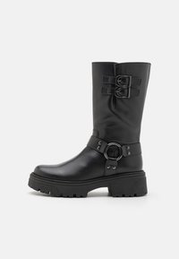 Bota de cuero negro hasta la rodilla con correas de doble hebilla, acento de hardware circular, suela robusta y textura suave; presenta una punta redondeada.