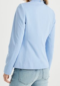 Ljusblå skräddarsydd kavaj med en mjuk textur, strukturerade axlar och en figurnära design, med en sömlös baksidan och utan synlig hårdvara.