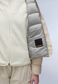 Gestreepte dubbel-laags jack met een crèmekleurige fleece-buitenkant en een lichtgrijze binnenvoering met matte afwerking. Inclusief zwart logopatch op de mouw.