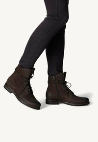 Bottines en cuir marron avec lacets et fermeture éclair, dotées d'une pointe arrondie et d'une finition texturée, assorties à un jean skinny noir.