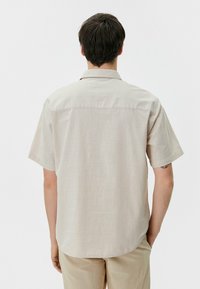 Lichtbeige shirt met korte mouwen, voorzien van een subtiele structuurpatroon, een klassieke kraag en een rechte zoom, gedragen met lichtgekleurde broek.
