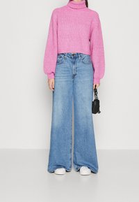 Pull à col roulé côtelé rose associé à un jean bleu à jambes larges. Le pull est doté de manches bouffantes ; le jean présente une coupe décontractée et un lavage clair.