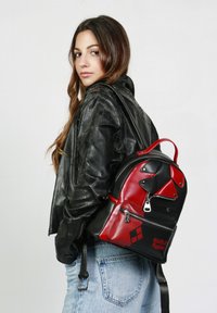 Mochila de cuero negra y roja con diseños geométricos, un compartimento principal con cremallera y un bolsillo frontal con el logo de Harley Quinn.