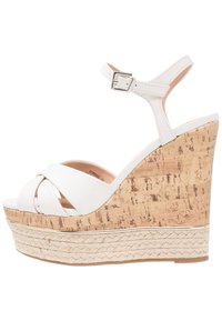 Sandalo con zeppa in pelle bianca, design a strappo incrociato, pianta in sughero e dettaglio in juta intrecciata. Fascetta alla caviglia regolabile con fibbia argento.