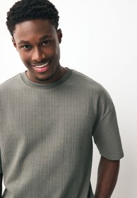 Kaki olijfgroene korte mouwen T-shirt met een gestructureerd, geribd ontwerp. Ronde hals met subtiele variaties in het stofpatroon.