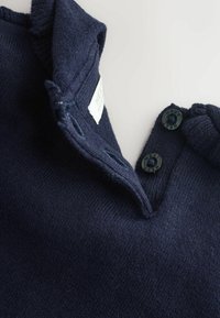 Marineblå strik-polo med folded krave, der har to sorte knapper og et lille mærke inde i kraven. Blød tekstur.