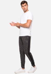 Vit t-shirt och svarta joggers med texturerad yta, med svarta sidostråk och en subtil logotyp, parat med vita sneakers.