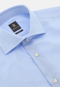 Svetlo modra, ožja pletena srajca z teksturirano tkanino, s koničastim ovratnikom in dvema belima gumboma spredaj ter etiketo blagovne znamke blizu ovratnika.