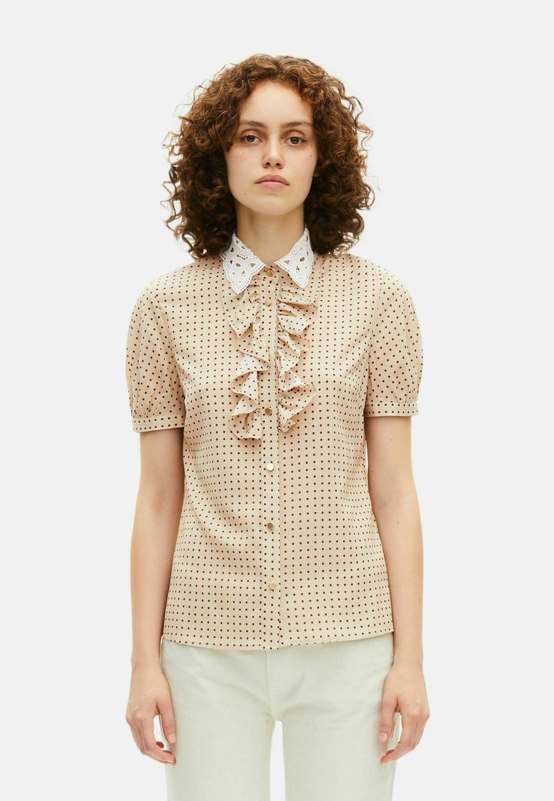 Beige shirt met korte mouwen met een gerimpelde voorkant, polkadotpatroon in bruin en een witte lace kraag. Voorkant knoopsluiting en een soepele textuur.