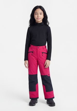 Barn som står vendt fremover iført svart langermet genser, røde og svarte vinterbukser med glidelåslommer, og svarte vintersko på hvit bakgrunn.