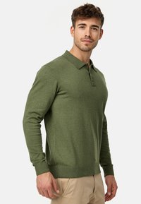Polo de manga larga verde hecho de una suave tela, con cuello, tapeta de tres botones y puños y dobladillo de canalé.
