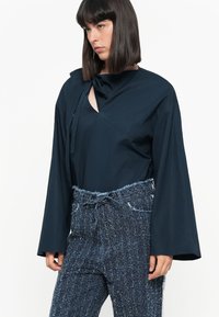 Navy blue blouse with a bow detail and a scoop neckline, paired with textured blue tweed pants featuring a drawstring waist and frayed hem.