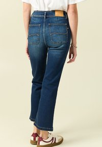 Granatowe dżinsy o wysokim stanie, proste nogawki, widoczne przeszycia, dwie tylne kieszenie oraz brązowa skórzana metka w talii.