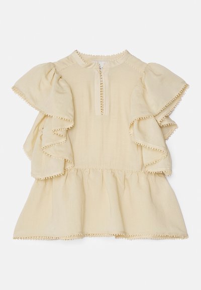 Lys beige topp med volanger på korte ermer, rund hals og glidelås foran. Har dekorativ pom-pom kant langs kantene.