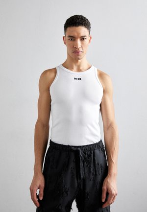 Débardeur blanc côtelé avec un col rond, arborant un logo noir. Porté avec un short noir usé, présentant des bords effilochés.