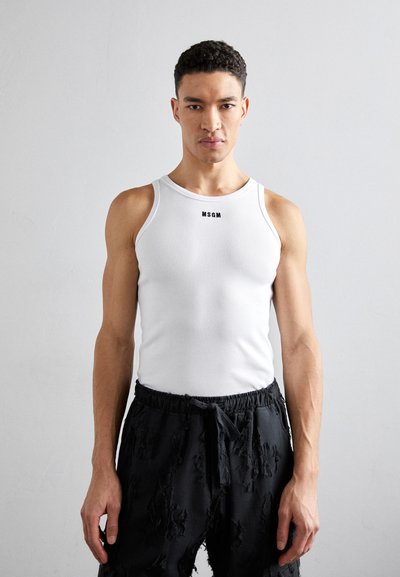Débardeur blanc côtelé avec un col rond, arborant un logo noir. Porté avec un short noir usé, présentant des bords effilochés.