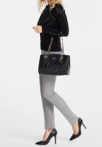 Musta käsilaukku kiiltävällä pinnalla ja ketjusangoilla, yhdistettynä mustaan niittipaitaan, harmaisiin ruutuhousuihin ja mustiin korkokenkiin.