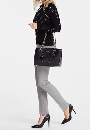 Sort håndtaske med en skinnende overflade og kædetræk, parret med en sort sweater med nitter, grå ternede bukser og sorte høje hæle.