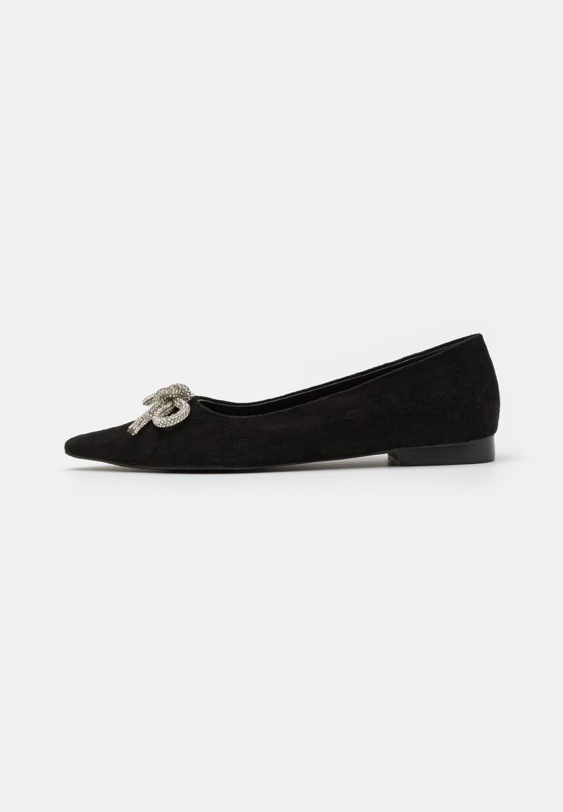 Chaussure plate en suede noir avec un bout pointu, ornée d'un détail de nœud en argent décoratif à l'avant, présentant un petit talon.
