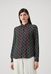 Košulja na dugih rukava u crnoj tkanini s geometrijskim uzorkom u narančastoj, zelenoj i plavoj boji. Dugih rukava s dugmadima na manžetama i ovratnikom.