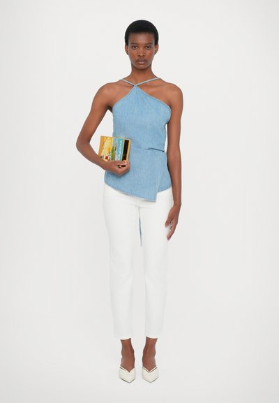 Denim halter top with cross straps, paired with white fitted trousers and pointed white heels. Model holding a colorful book.