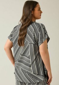 Top a maniche corte bianco e nero a righe, con una vestibilità ampia, caratterizzato da righe di larghezza variabile e motivi geometrici sul retro.