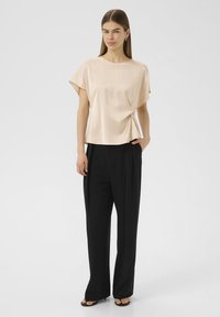 Haut en soie pâle avec des manches courtes, détail noué sur le côté, associé à un pantalon noir taille haute à jambes larges et des sandales noires.