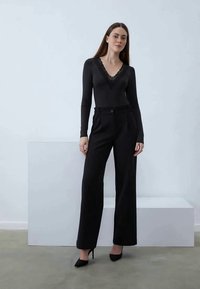 Black long-sleeve bodysuit with a lace v-neckline paired with high-waisted, wide-leg black trousers and stiletto heels.