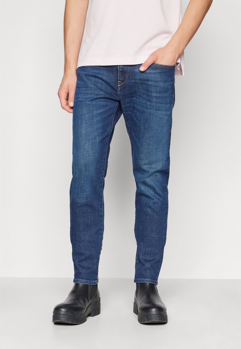Jean denim bleu coupe slim, avec un classique design à cinq poches et une légère décoloration. Associé à des bottines noires.