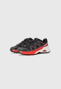 Black and red athletic shoes featuring a textured upper, bold cut-out design, a cushioned midsole, and rugged outsole for traction.